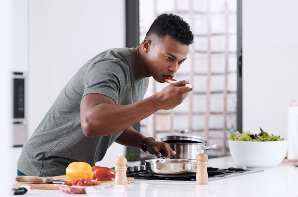 a man tastes some of the soup he is preparing at a stovetop